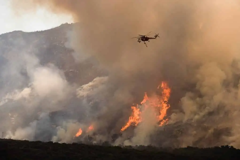 Helicopter battling a fierce wildfire amidst smoke and flames.